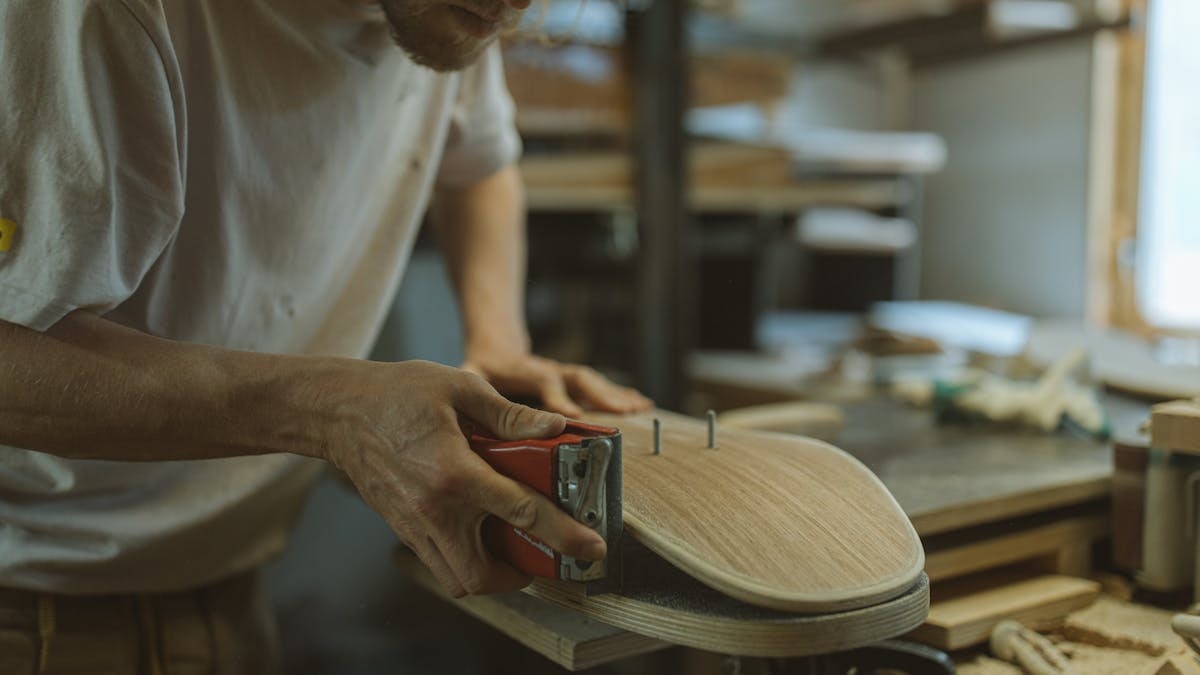 Close-up of a craftsman sanding a skateboard in a home workshop environment.